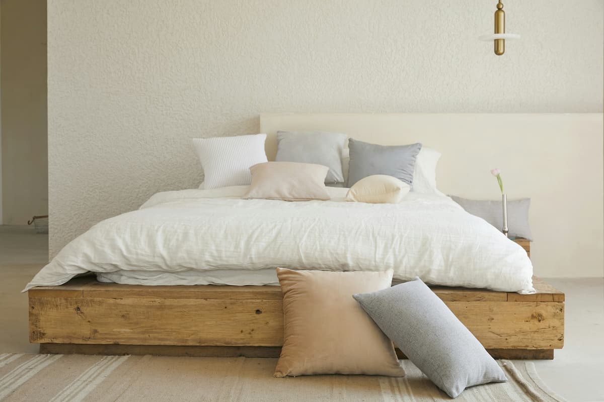 Quarto com cama de casal decorada em tons neutros, roupas de cama e almofadas organizadas, ilustrando itens comuns de uma lista de enxoval de casamento.