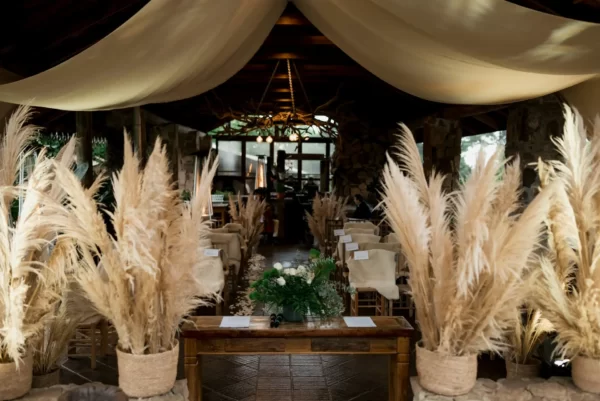 Decoração de um casamento boho chic. Imagem de um corredor com cortina bege e plumas.