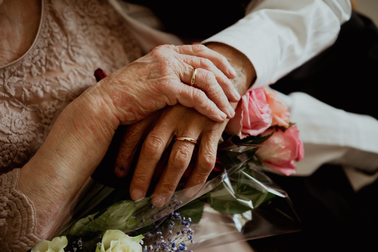 A imagem mostra as mãos de um casal idoso usando alianças.