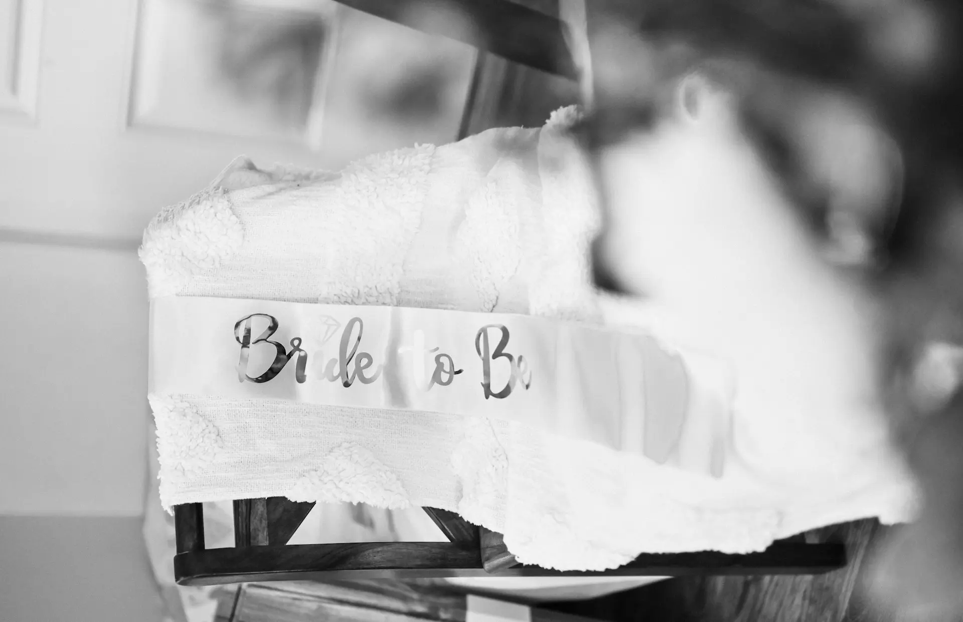 Toalha branca com faixa “Bride to Be” sobre cadeira, em preparação para o casamento.