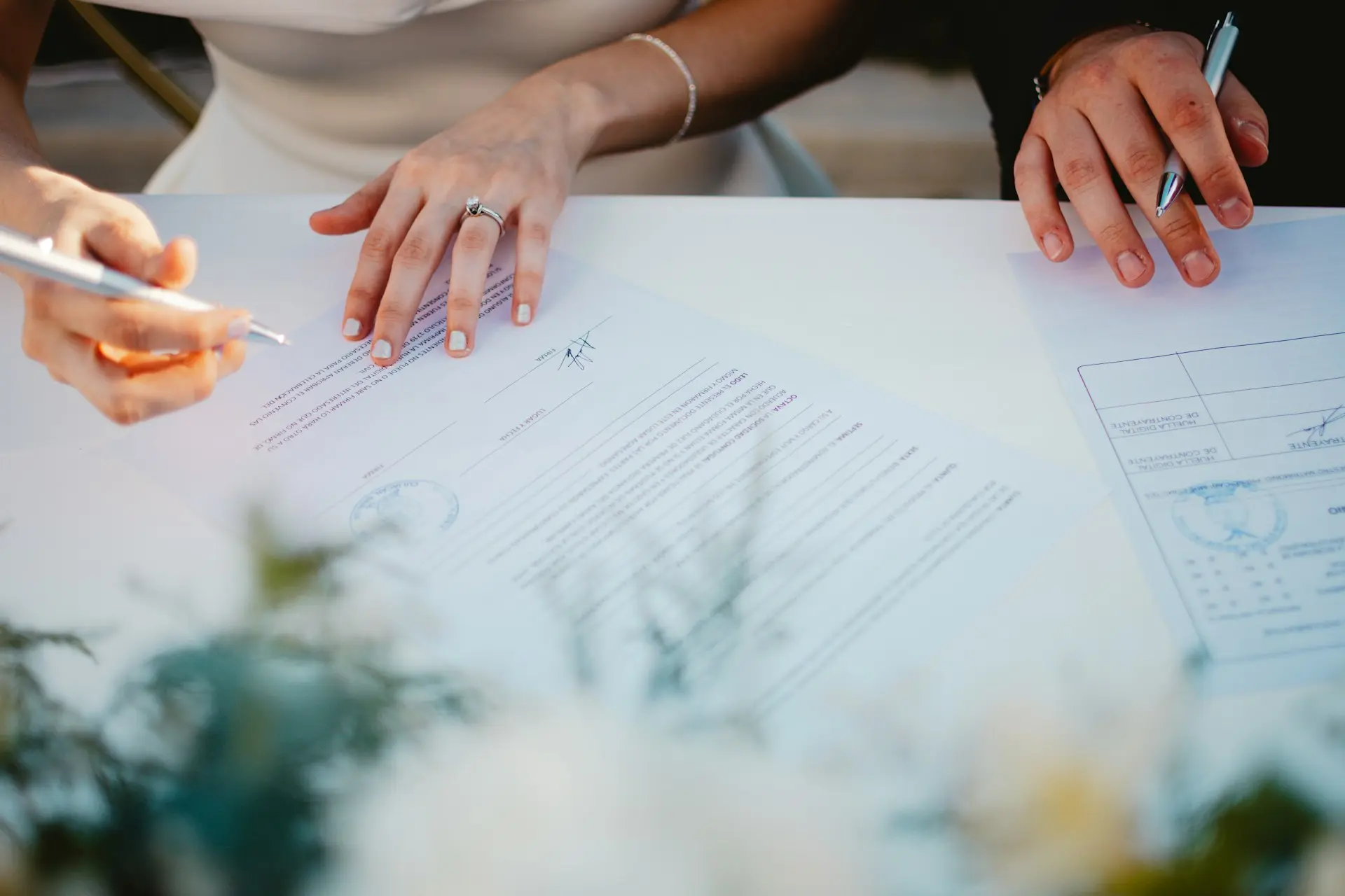 Imagem de um casal assinando documentos no casamento civil, em uma mesa simples, com caneta em mãos e clima formal.