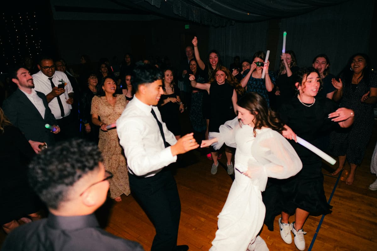 Noivos dançando animados no centro da pista enquanto convidados comemoram ao redor, ilustrando a escolha de músicas para casamento animar a festa.