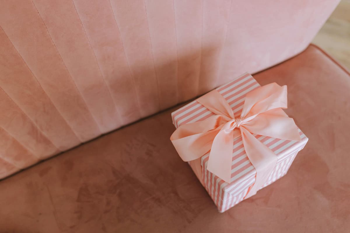 Caixa de presente decorada com laço rosa sobre um sofá, representando uma opção simples e elegante de presente de última hora de casamento.