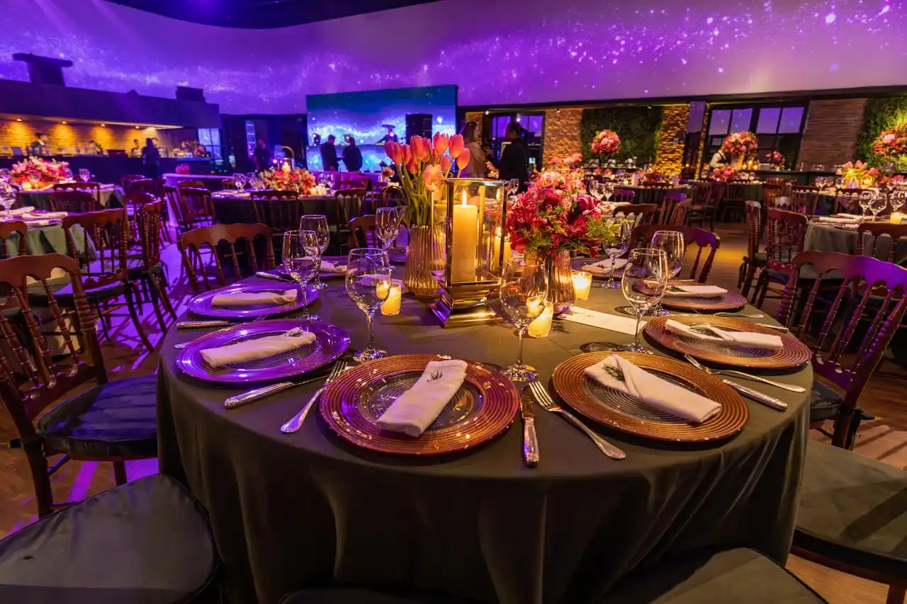 Como montar um jantar de casamento elegante e bem estruturado? Imagem mostra mesa de evento elegante, com flores, velas e iluminação roxa em ambiente sofisticado.
