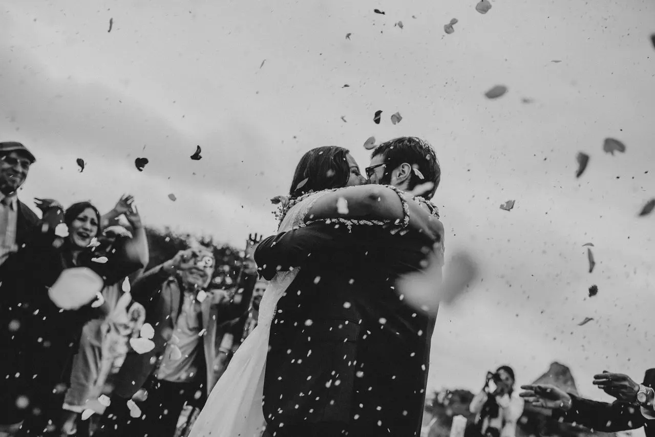 Resgate da lista de presentes: o que é, como funciona e quando solicitar? Casal de noivos se abraçando durante a cerimônia de casamento enquanto convidados celebram ao redor.