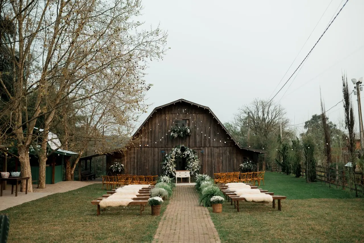 Ideias para site de casamento rústico e personalizado Cerimônia de casamento rústica ao ar livre, com bancos de madeira, flores brancas e celeiro ao fundo.