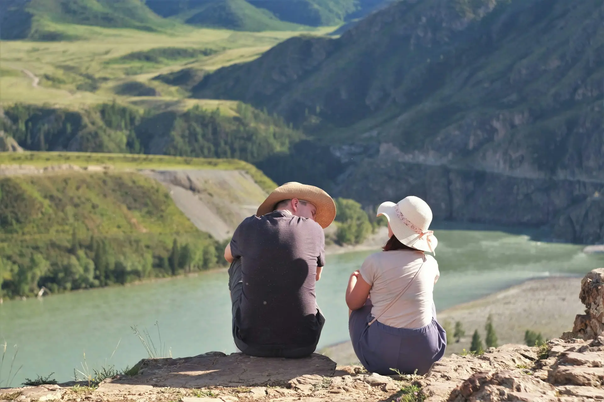 Homem e mulher sentada em rocha próxima a um lago em paisagem natural