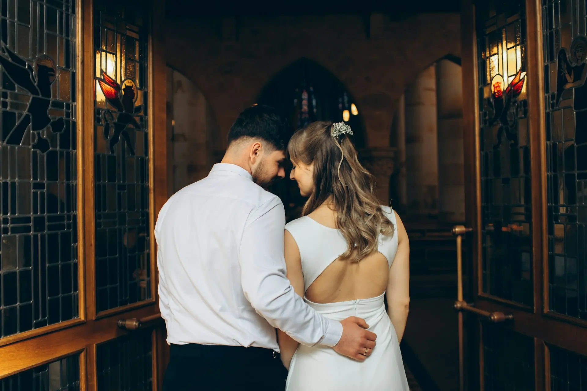 Casal de noivos abraçado na entrada de uma igreja, momentos antes ou depois da cerimônia de casamento.