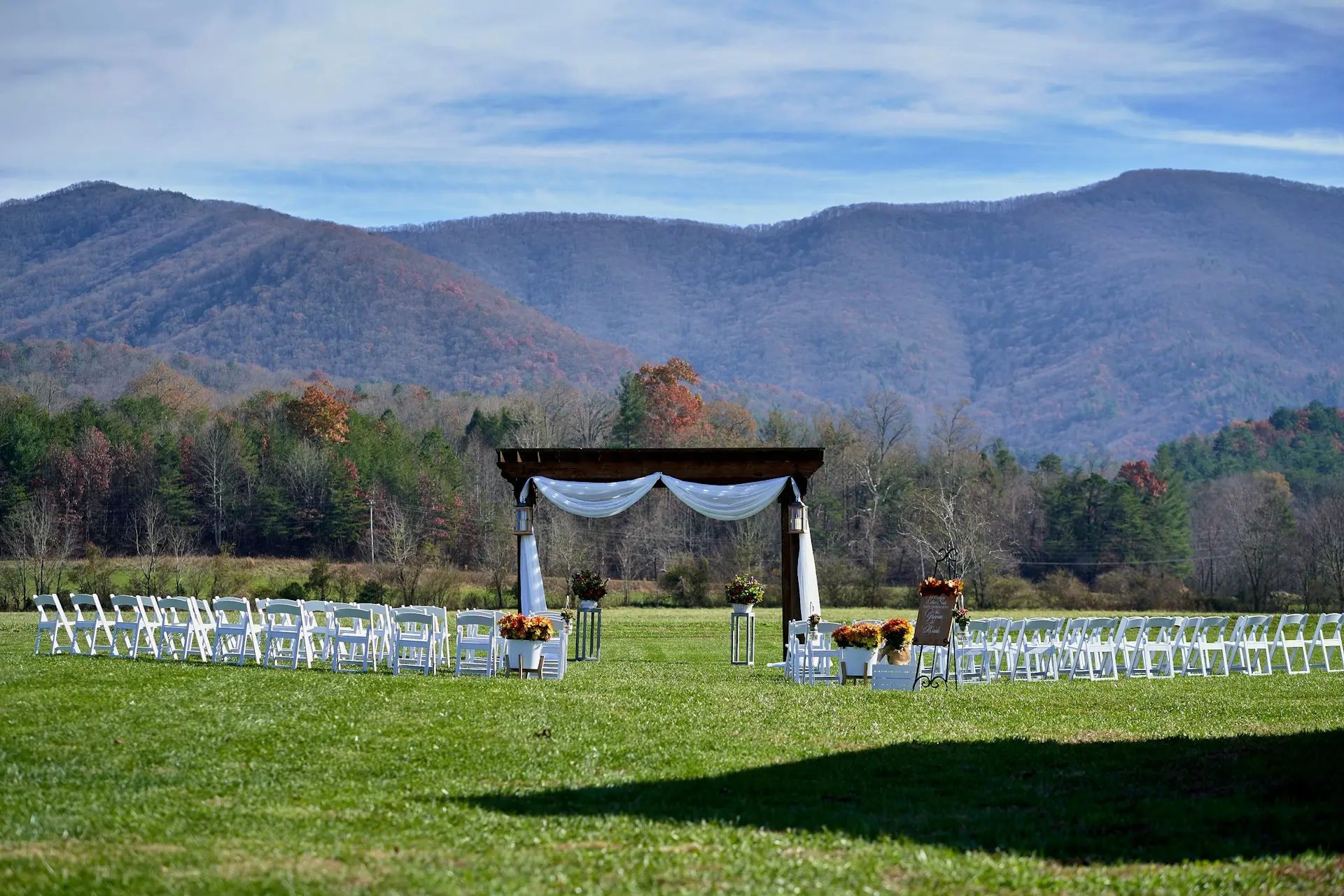 casamento-montanha Espaço para casamento ao ar livre com vista para as montanhas, gramado, cadeiras brancas e altar de madeira decorado com tecidos e flores.
