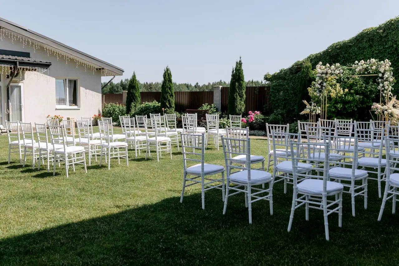 casamento-no-quintal Espaço para casamento no quintal de casa, com cadeiras brancas organizadas sobre o gramado e altar decorado com flores em um jardim.