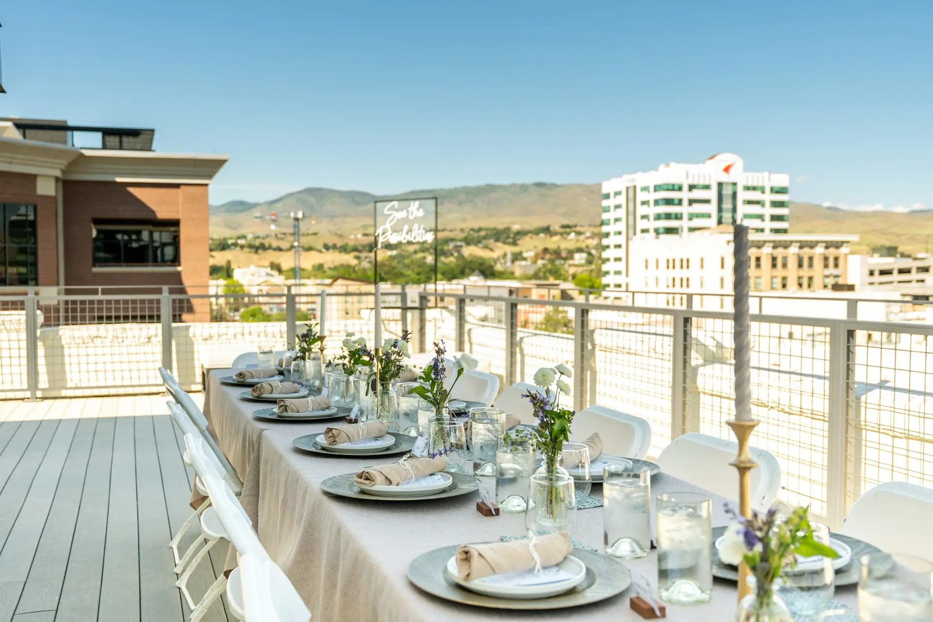 casamento-rooftop Mesa decorada para casamento em rooftop, com vista urbana e montanhas ao fundo, cadeiras brancas, arranjos florais e ambientação ao ar livre.