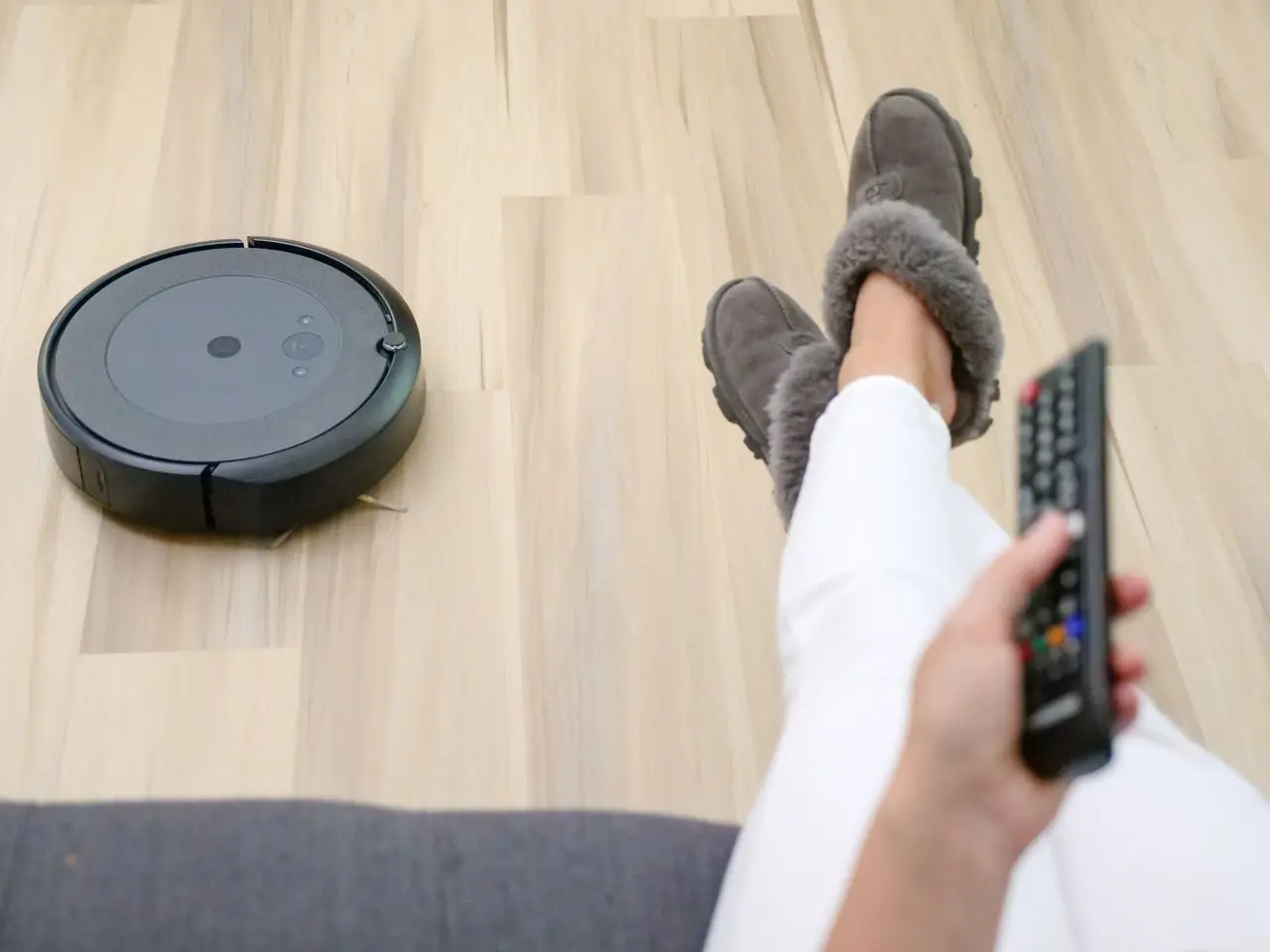 Pessoa relaxando em casa enquanto um robô aspirador limpa o piso.