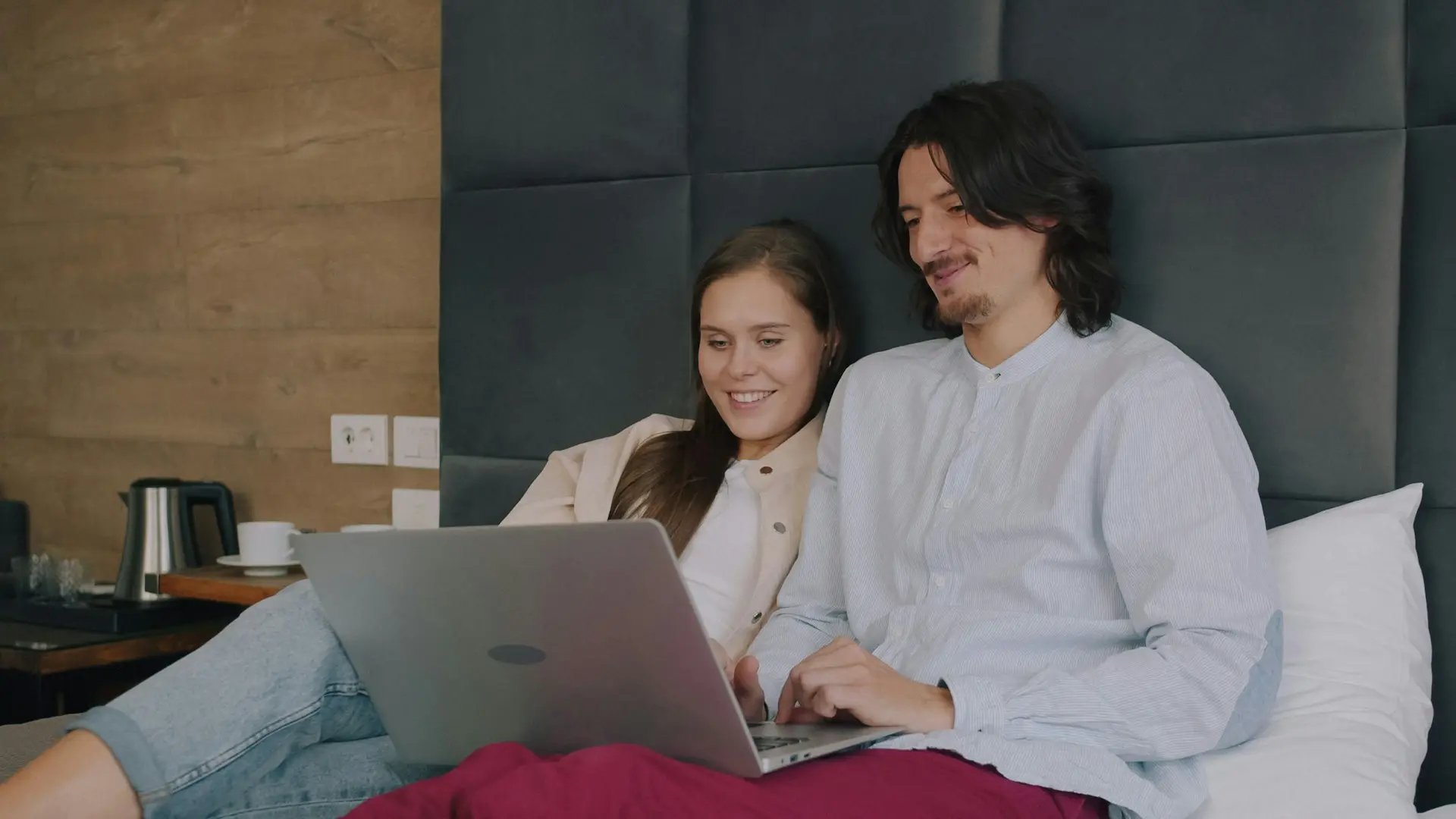 Casal usando um notebook enquanto relaxa na cama de um quarto.