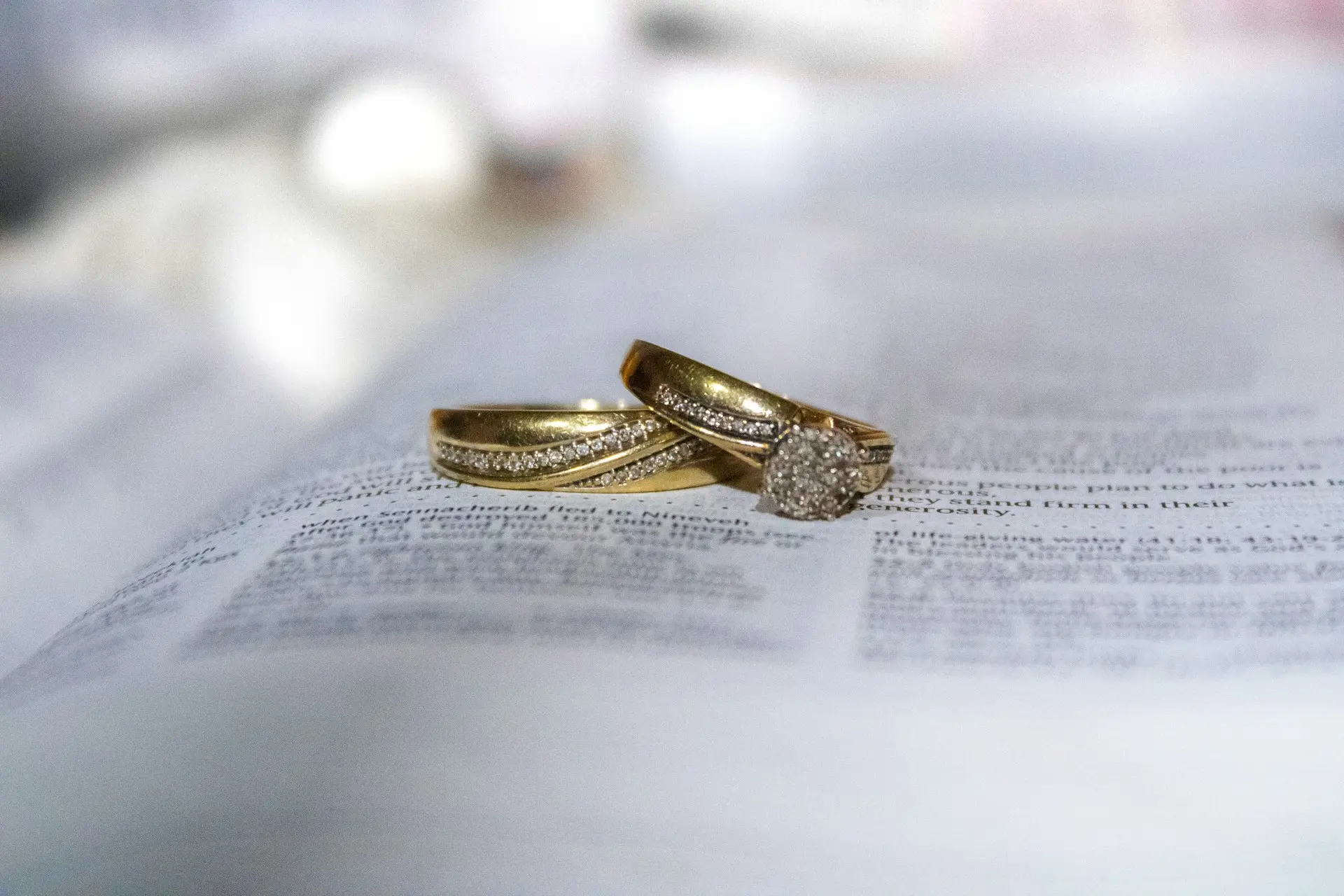 Duas alianças de casamento douradas, uma delas com pedras brilhantes, apoiadas sobre as páginas abertas de uma Bíblia.