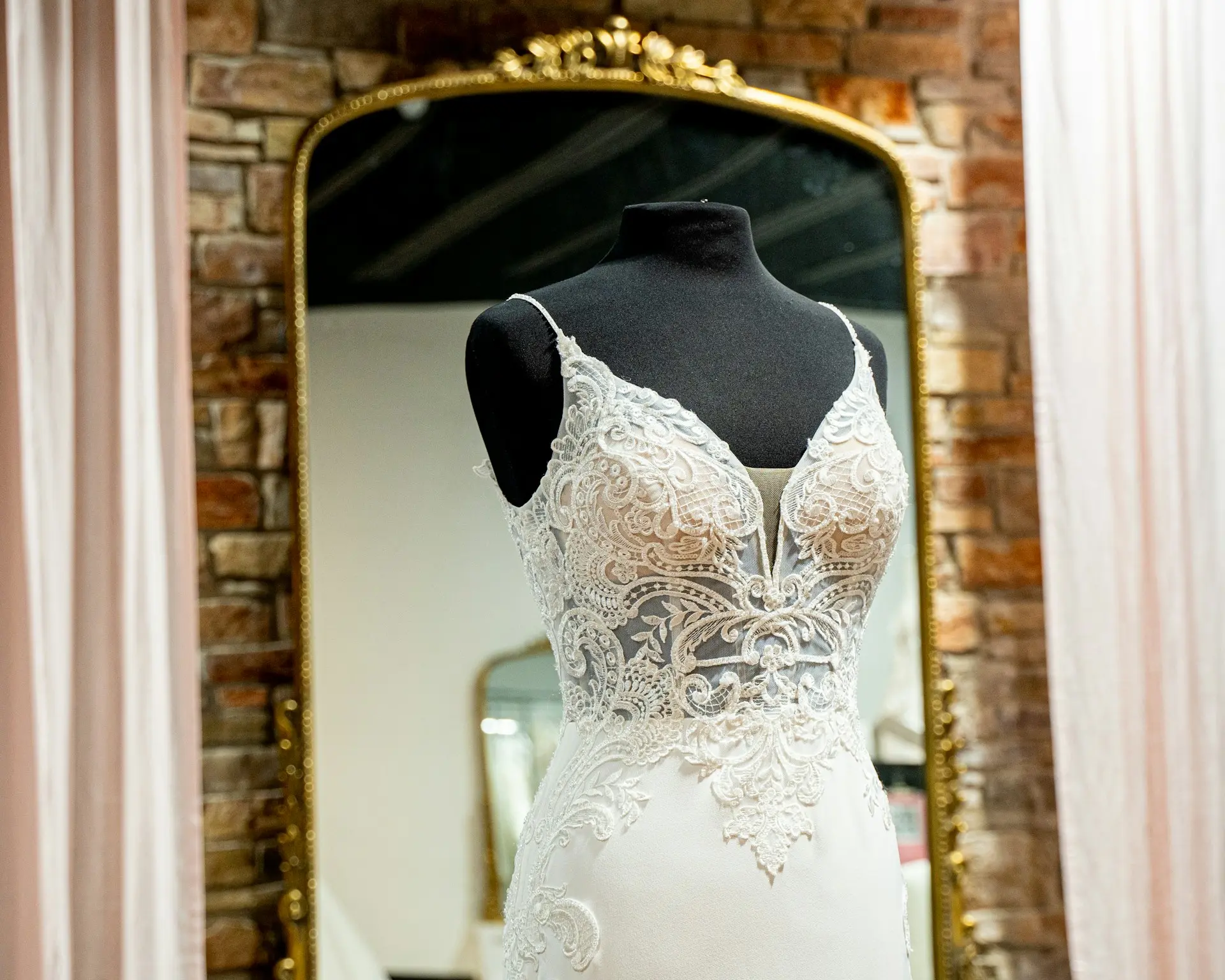 Detalhe de vestido de noiva rendado branco em manequim, com alças finas, decote em V e corpete transparente com aplicações de renda floral.