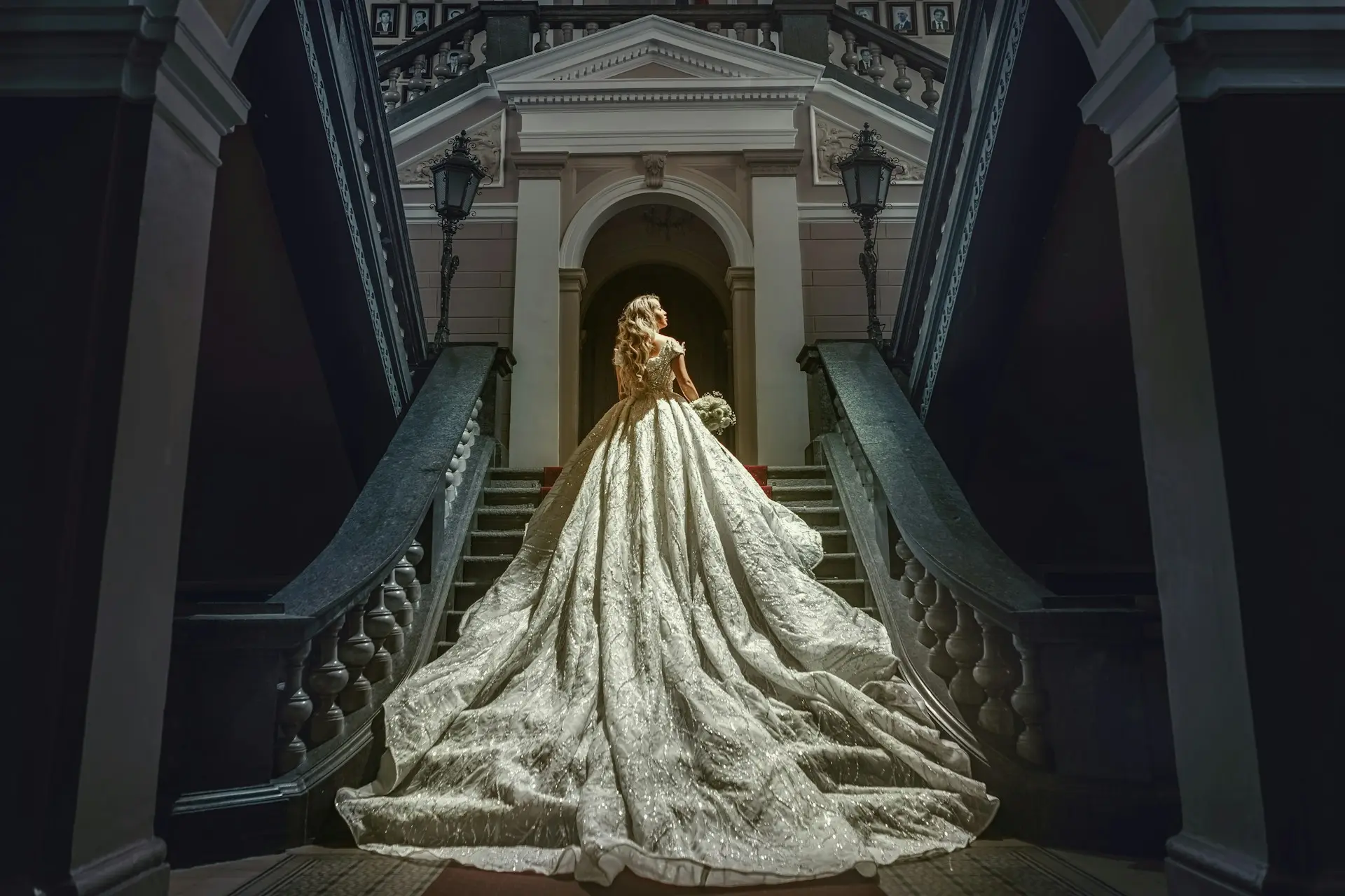 Noiva com vestido de casamento princesa, corpete ajustado, saia volumosa bordada e cauda longa, posando em uma escadaria clássica.